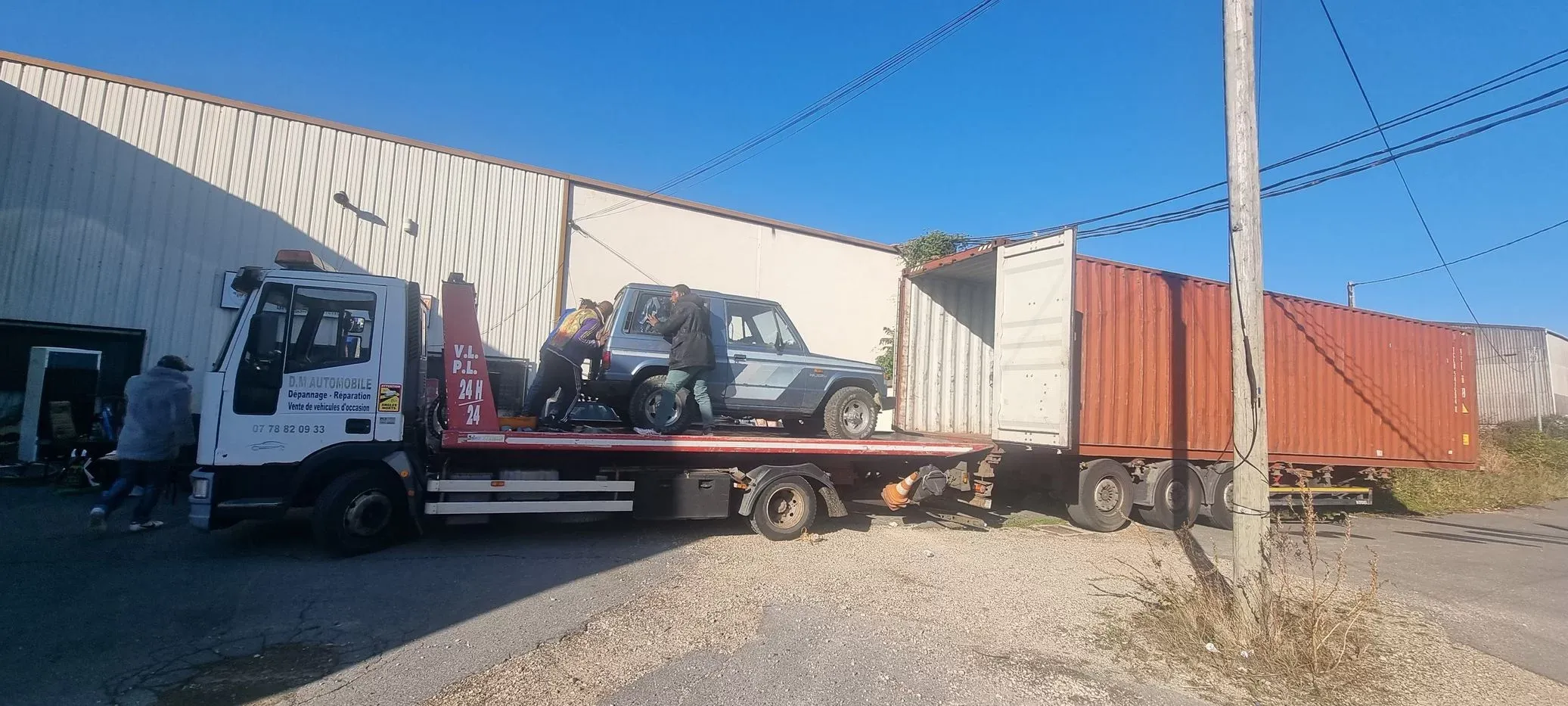 Chargement d'un 4x4 sur camion plateau devant un conteneur